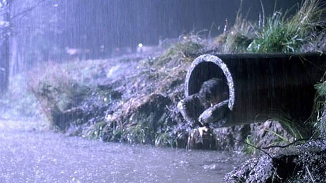 Dark night time scene. man covered in filth crawling out of sewage pipe into rancid brown water